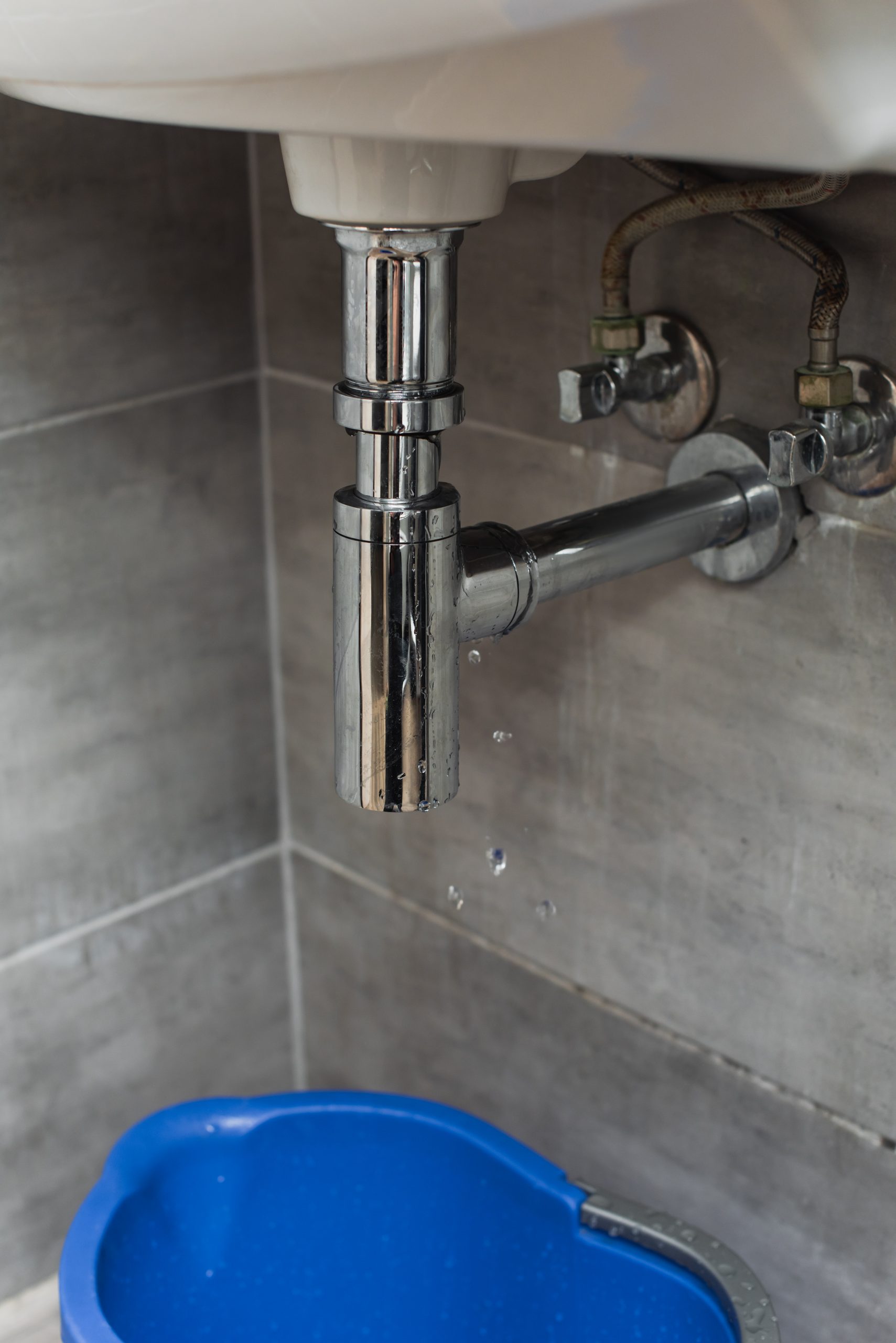 Blue bucket standing in bathroom under leaking pipe